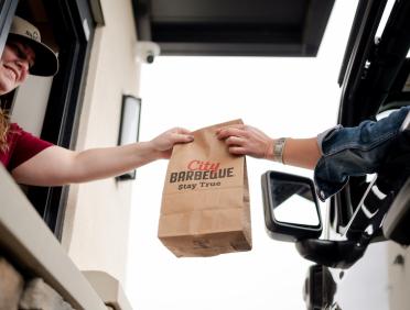 Handing over a City Barbeque bag in the drive-thru